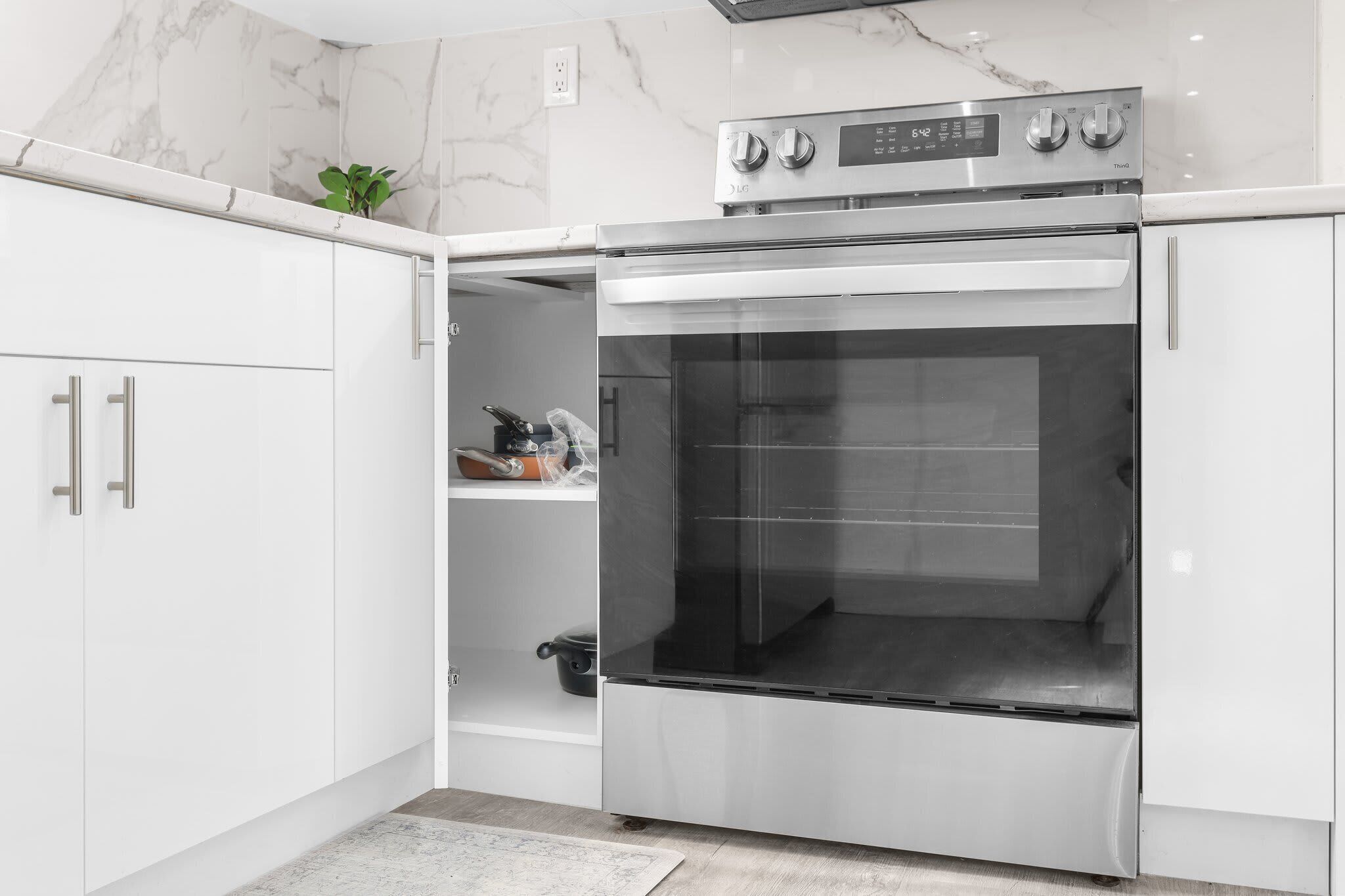 A modern kitchen with white cabinetry, a stainless steel oven, and a marble backsplash.