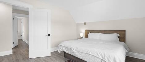 A bedroom with a large bed, a wooden headboard, a nightstand with a lamp, and a patterned rug.