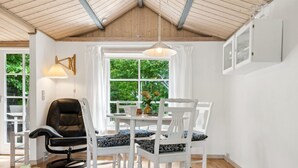 A dining area with a wooden ceiling, white walls, and a large window with a view of greenery. There are white chairs with patterned cushions and a black chair. - "Konrad" - 270m from the sea by Interhome (Nexø)