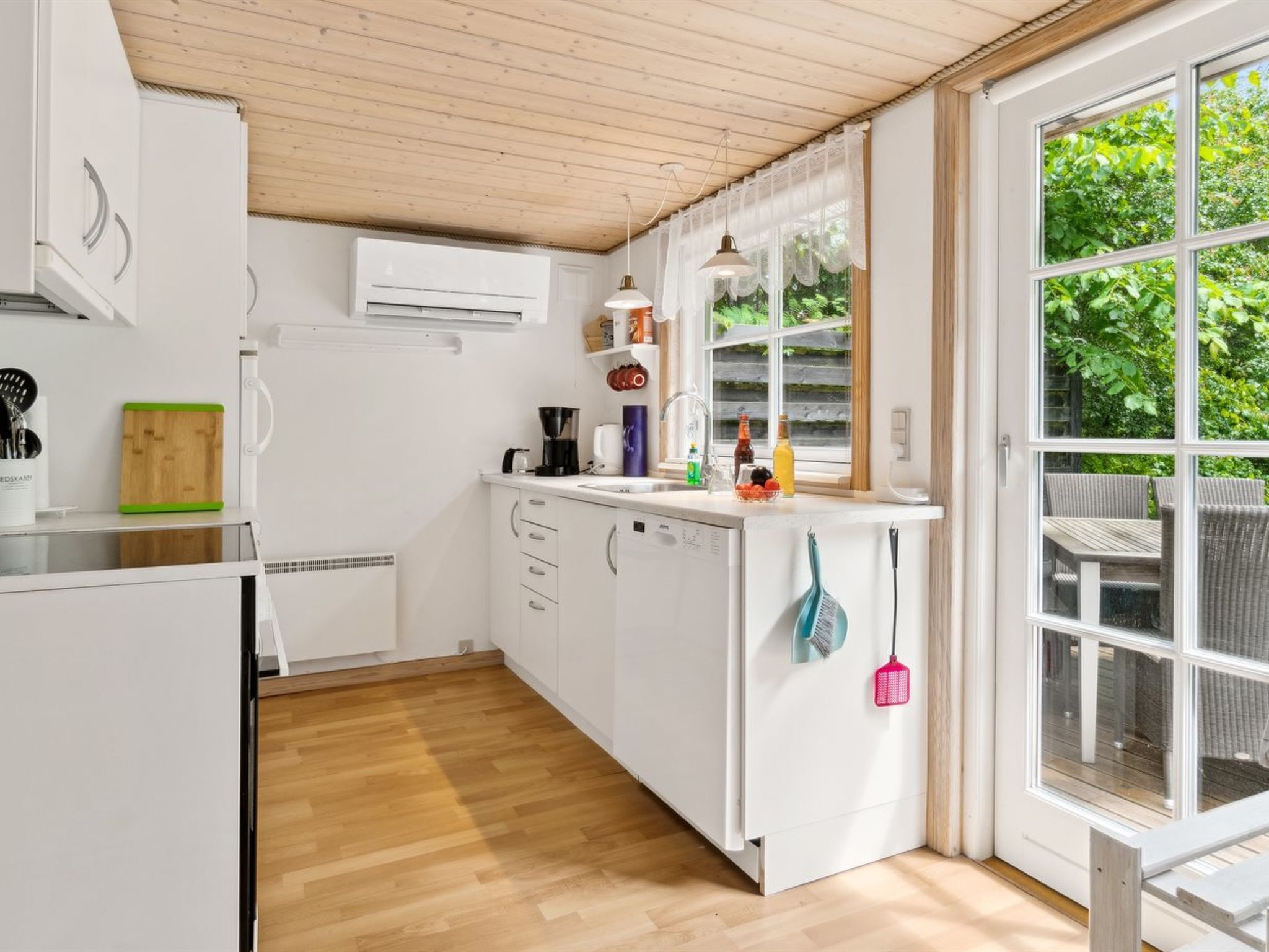 A modern kitchen with white cabinets, a wooden floor, and a large window with a view of greenery.