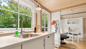 A modern kitchen with a large window, a sink, and a dining area with white furniture. - "Konrad" - 270m from the sea by Interhome (Nexø)
