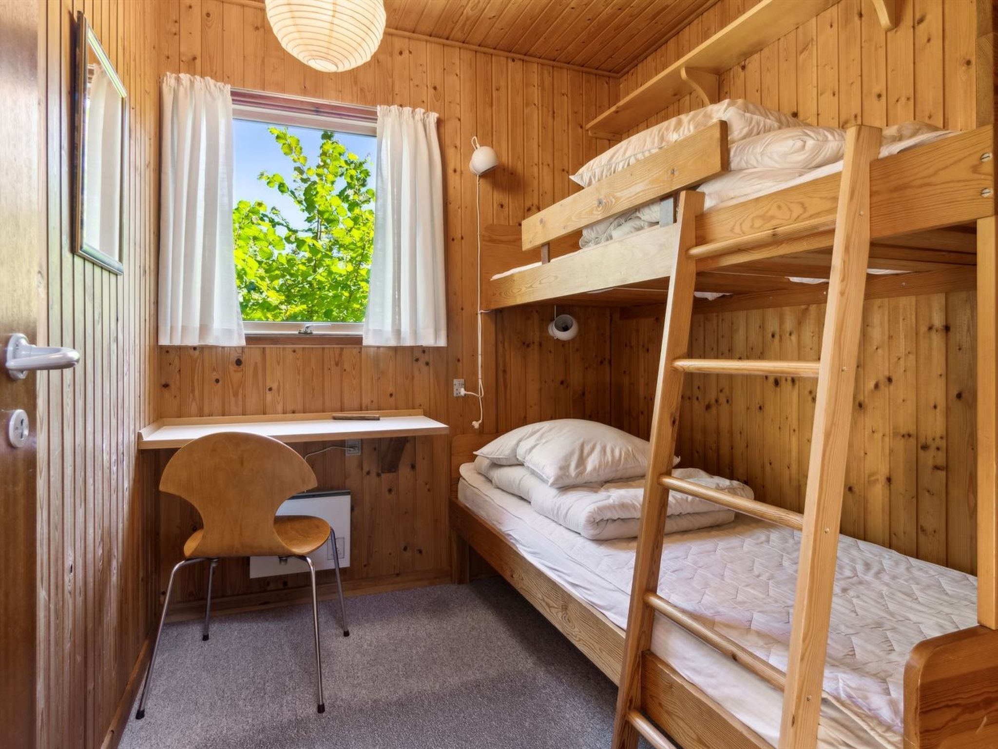 A compact wooden room with bunk beds, a desk, and a chair.