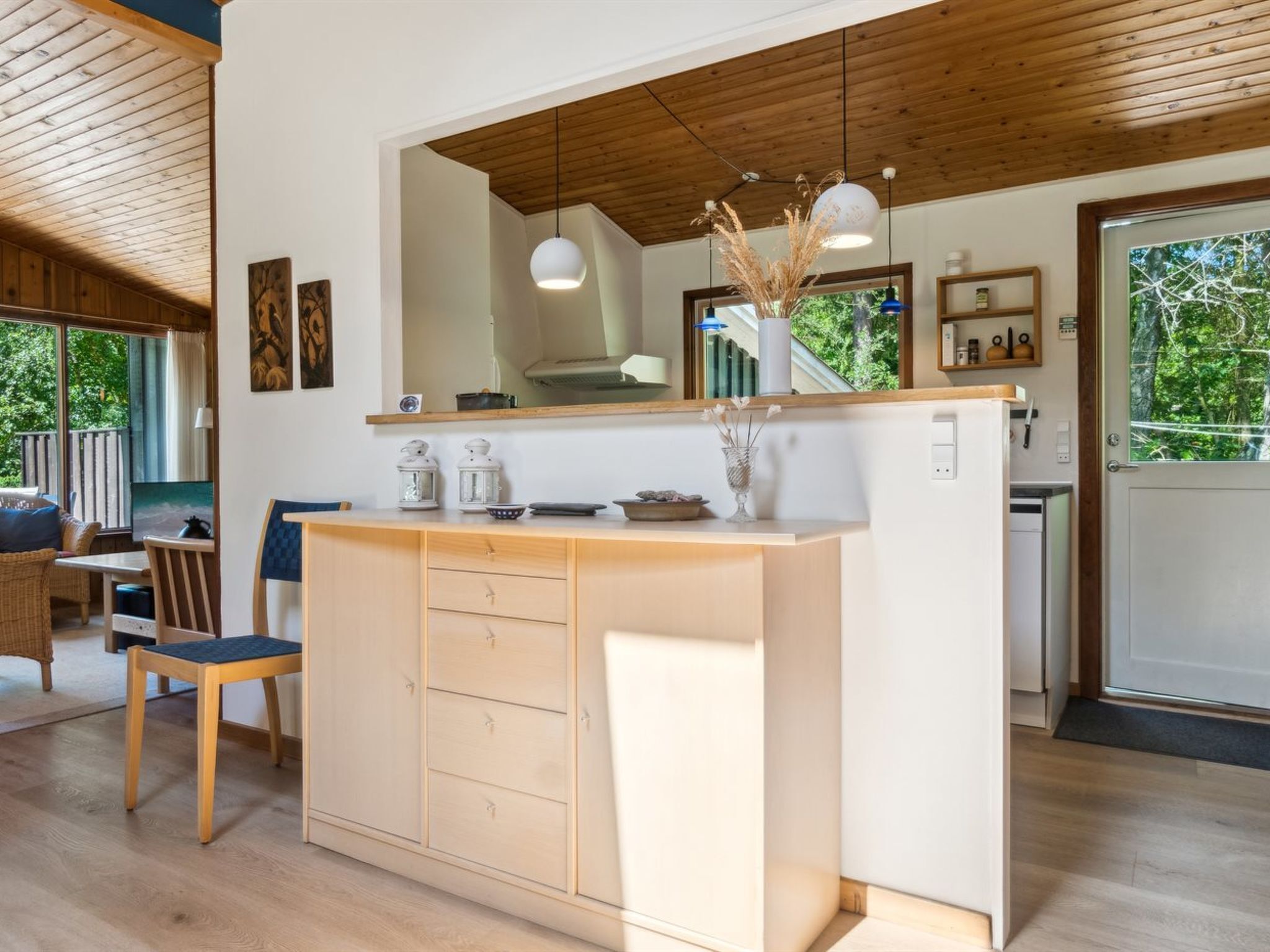 A modern kitchen with wooden cabinets, a central island, pendant lights, and a view of the outdoors.