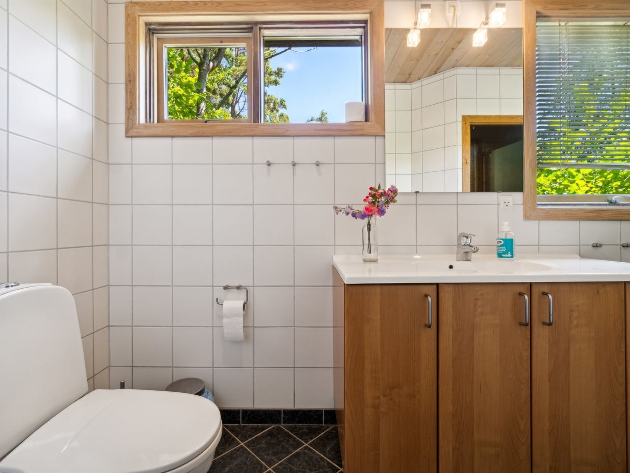 Une salle de bain comprenant des toilettes, un lavabo avec un miroir et une fenêtre donnant sur des arbres.