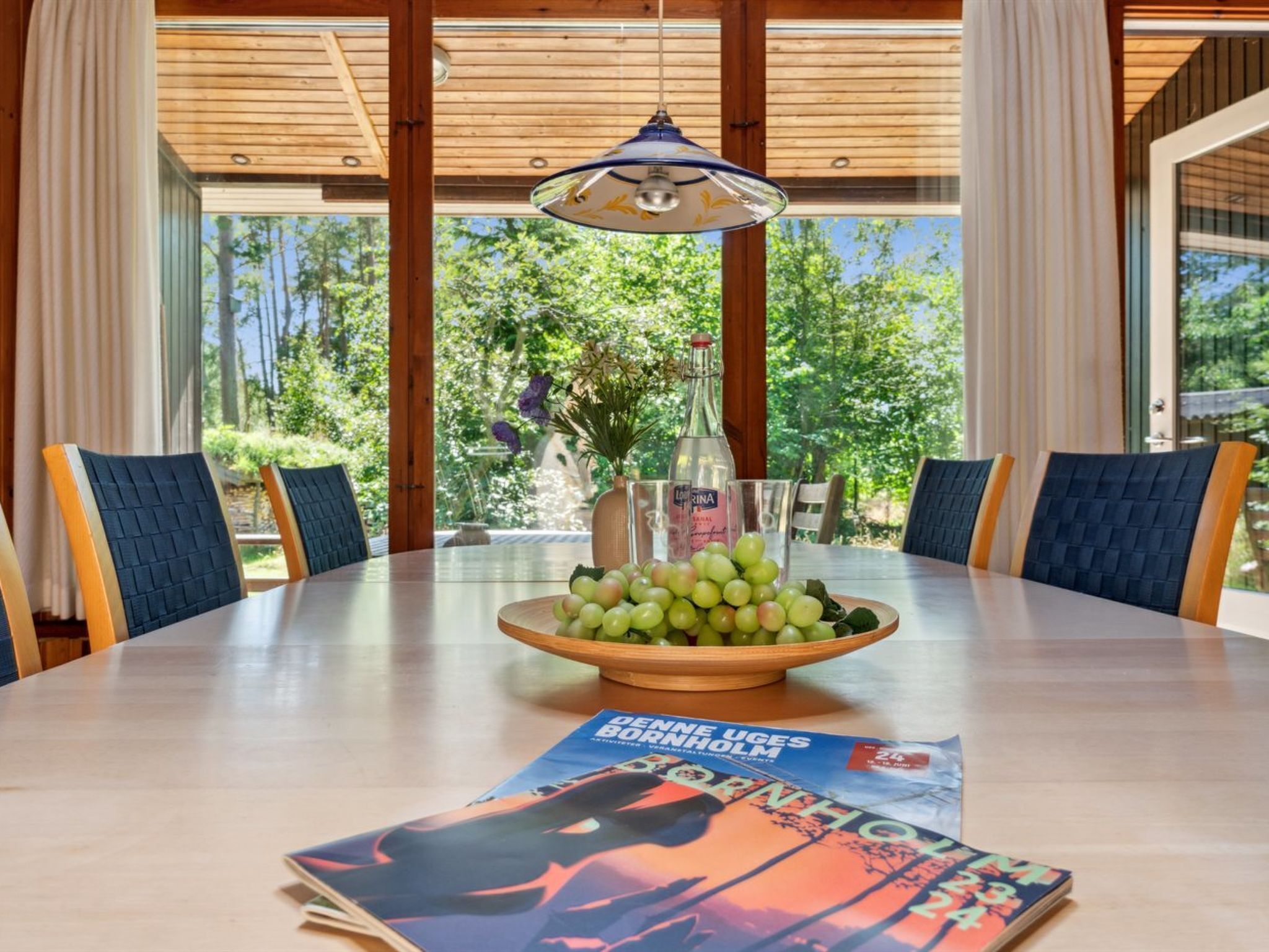A round dining table with a bowl of green grapes, a bottle, and a magazine.