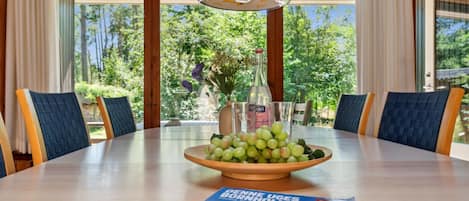 A round dining table with a bowl of green grapes, a bottle, and a magazine.