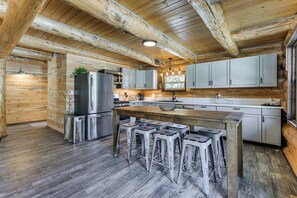 A rustic kitchen with wooden beams, a stainless steel refrigerator, and a bar area with stools.