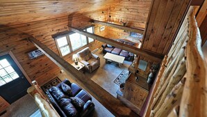 Una cabana amb interior d'estil loft, que inclou una zona d'estar amb un sofà, una taula de centre i una llar de foc. Hi ha una zona de menjador amb una taula i cadires, i una cuina amb una pica i un taulell.