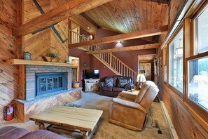Ein rustikales Blockhaus-Interieur mit Kamin, Holzbalken, einer Couch und einem Fernseher.