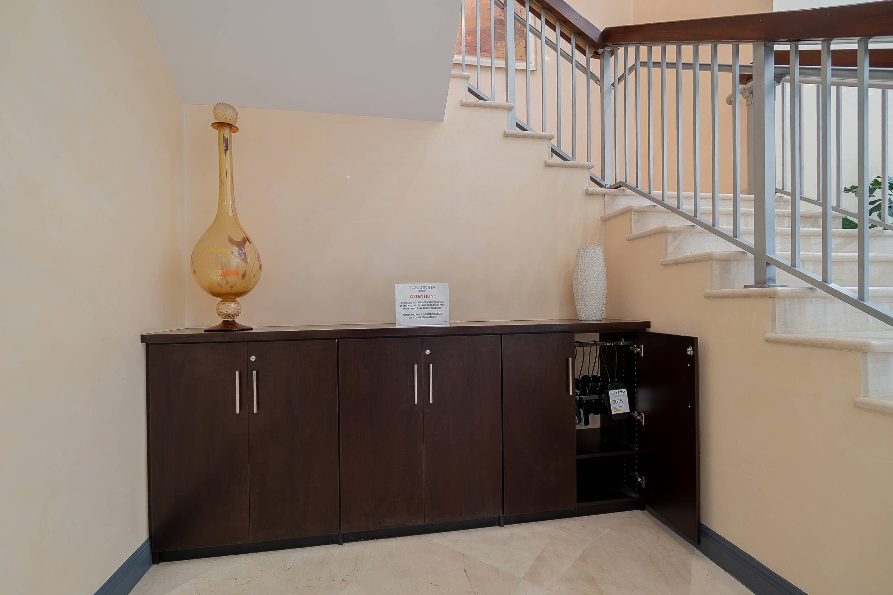 A staircase with a metal railing, a dark wooden cabinet with two doors, and a sign on the wall.