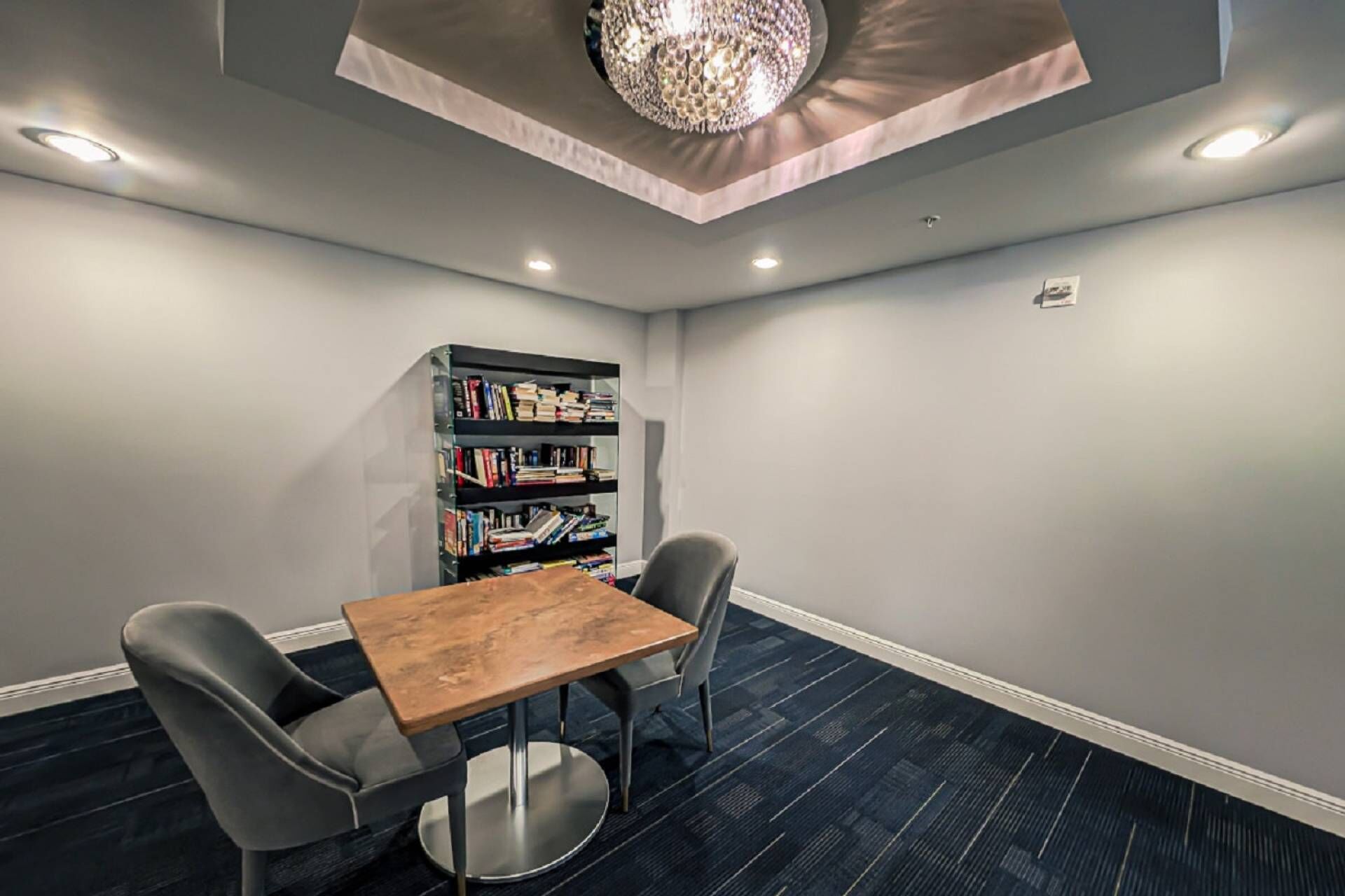 Une salle de conférence avec une table en bois, deux chaises, une bibliothèque et un lustre.