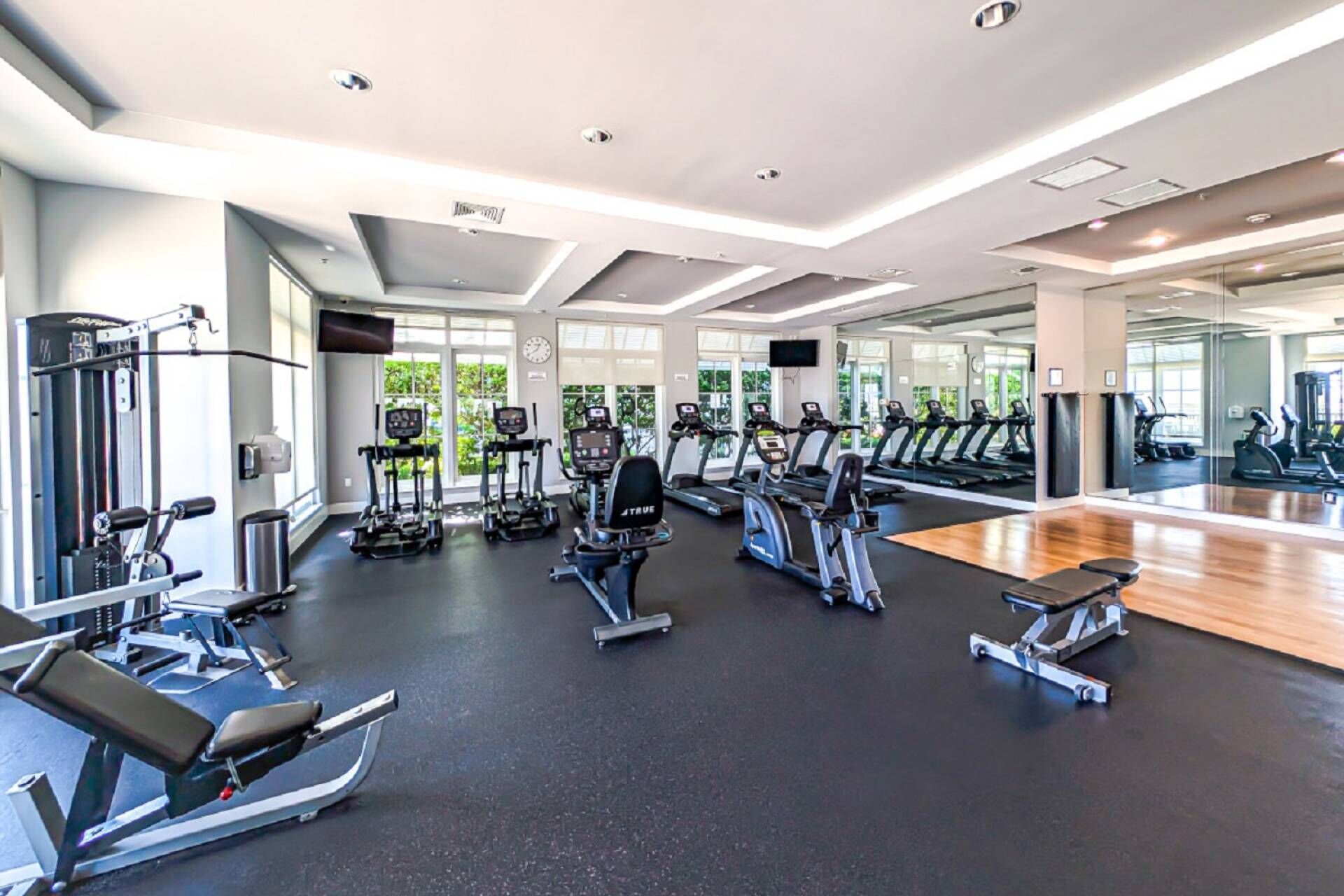 A gym with various exercise equipment, large windows, and a mirrored wall.