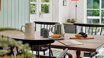 Une table en bois sur laquelle se trouvent une tasse blanche, une théière en argent et une assiette avec des biscuits et des raisins.