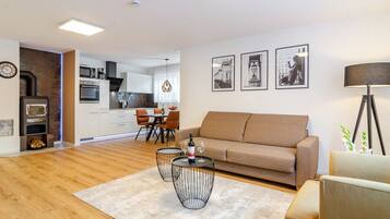 Ein modernes Wohnzimmer mit einer Couch, zwei Gestelltischen und einem Essbereich mit Stühlen.