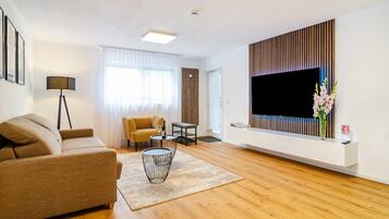 Ein modernes Wohnzimmer mit einer Couch, einem Couchtisch, einem Fernseher und einer dekorativen Vase.