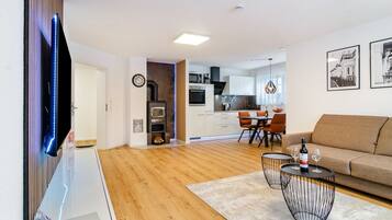 Una sala de estar moderna con un sofá, un comedor con sillas, una cocina equipada y un televisor montado en la pared.