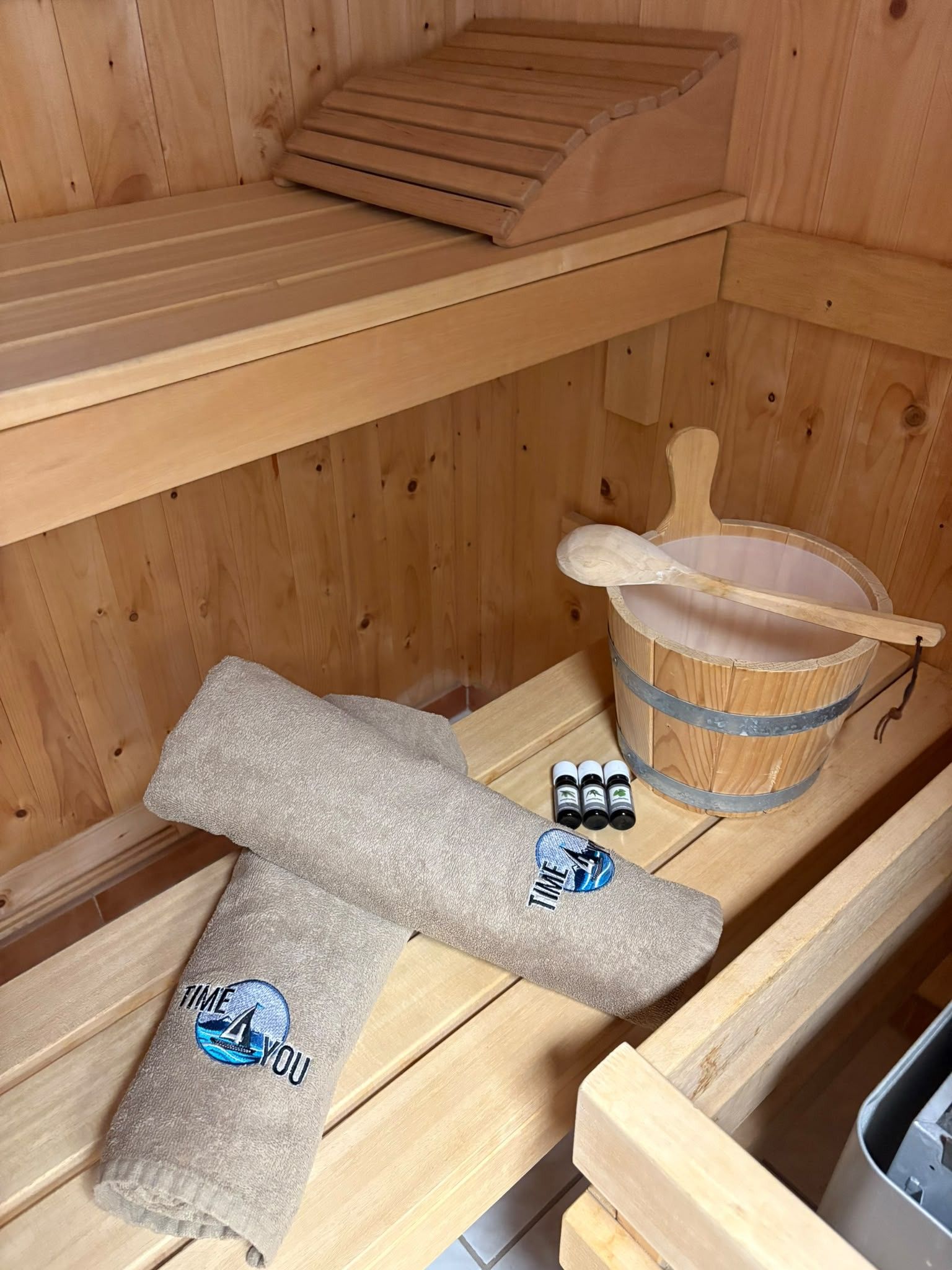 Eine Holzsauna mit einer Sitzbank, einem Holzeimer und einem Handtuch mit einem Logo.
