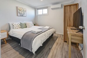 Quarto com cama, mesa de cabeceira e suporte para televisão.