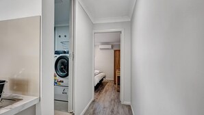 Un couloir étroit avec un lave-linge, un lit et une porte en bois.