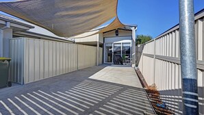 Un espace extérieur abrité, doté d’une voile d’ombrage incurvée, d’une clôture en métal et offrant une vue sur un ciel dégagé.