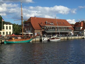 A harbor with boats docked, a building with a red roof, and a sign that reads 'EM. Scheel.' - Holiday Apartment 'Wohnanlage Am Mühlenteich' with Balcony and Wi-Fi (Timmendorfer Strand)
