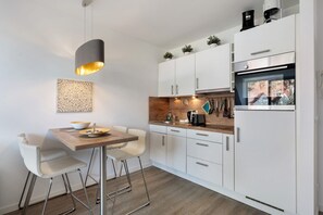 A modern kitchen with white cabinets, a wooden countertop, a hanging light fixture, and a window with a view. - Holiday Apartment 'Wohnanlage Am Mühlenteich' with Balcony and Wi-Fi (Timmendorfer Strand)