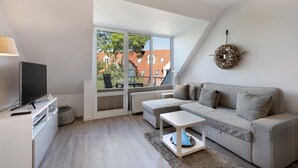 A modern living room with a sofa, a coffee table, a TV, and a large window with a view of buildings.