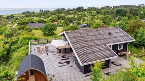 Ein modernes Haus mit einer Holterrasse, einem überdachten Sitzbereich und Blick auf eine Küstenlandschaft.