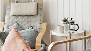 Ein gemütliches Zimmer mit einem Holzstuhl, einem kleinen runden Tisch mit einer Kaffeemaschine und einem Kissen auf dem Stuhl.