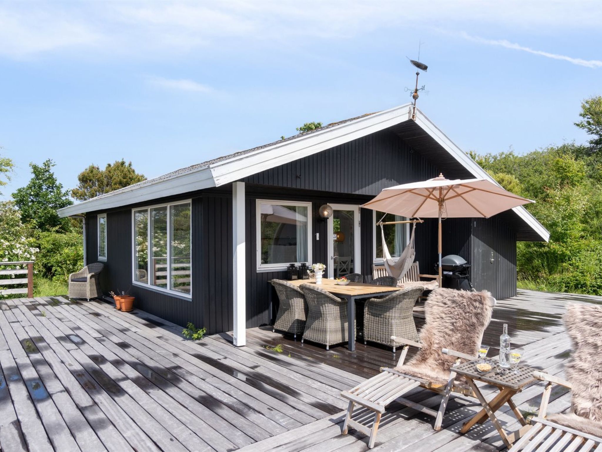 A modern cabin with a deck, outdoor seating, and a large umbrella.