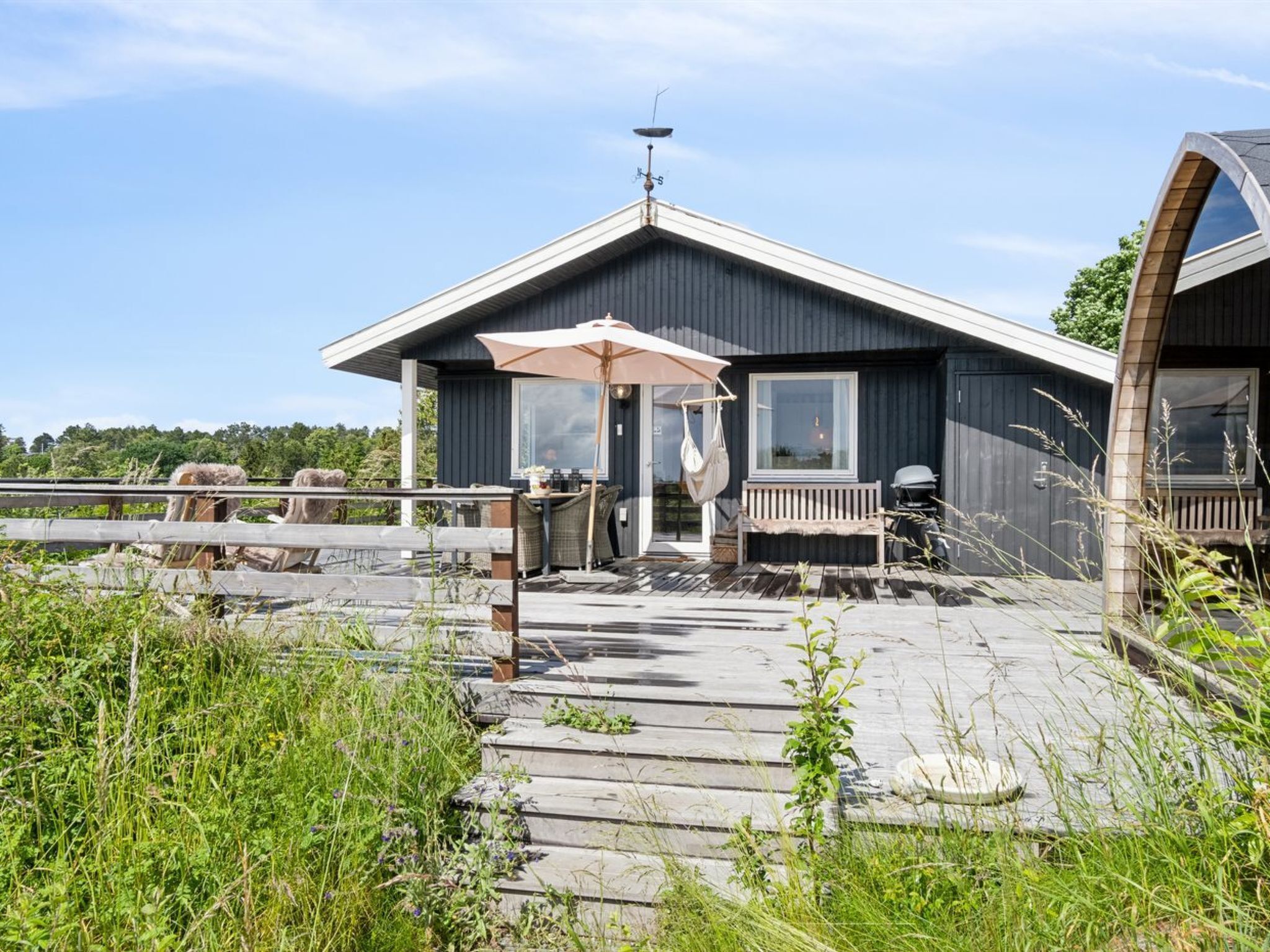 A modern cabin with a deck, a covered outdoor seating area, and a large window overlooking a natural landscape.