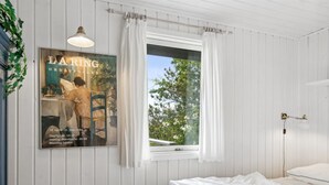 Ein Schlafzimmer mit Bett, einem Vorhangfenster, einer Wandlampe und einem Bild an der Wand.