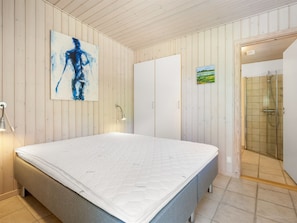 A bedroom with a bed, a painting, a wardrobe, and a shower area.
