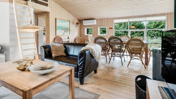 En rummelig opholdsstue med træloft, en sort lædersofa, et spisebord med stole og et fjernsyn.
