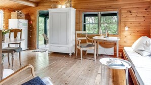 Een gezellig chalet binnen met houten wanden, een eethoek, een wit kastje en een bed.