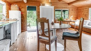 Een gezellig chaletinterieur met houten details, een eethoek met stoelen en een tafel, en een keuken met een koelkast en spoelbak.