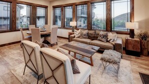 A spacious living room with a large window, a sofa set, a coffee table, and a dining area.