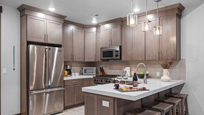 A modern kitchen with stainless steel appliances, wooden cabinets, and a central island with stools.
