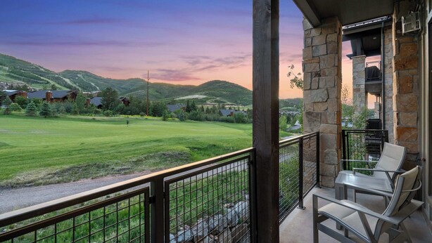 A balcony with a view of a green field and hills, stone pillars, and two chairs.