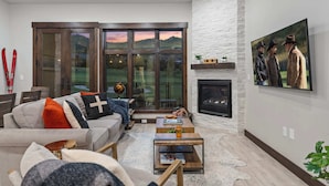 A modern living room with a fireplace, a large window with a scenic view, and a mounted TV.