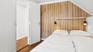 A bedroom with a sloped ceiling, wooden panel wall, two bedside lamps, a bed with white bedding, and a white door. - "Ardan" - 450m from the sea by Interhome (Ebeltoft)