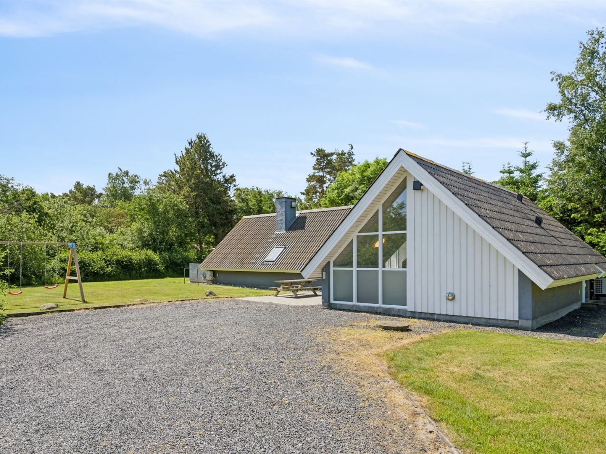 Un bâtiment moderne doté d’un toit en pente, de grandes fenêtres et d’une allée gravillonnée.