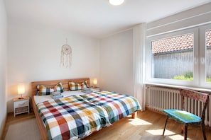 Une chambre à coucher comprenant un lit, une table de chevet, une lampe, une chaise, un radiateur et une fenêtre donnant sur un paysage agréable.