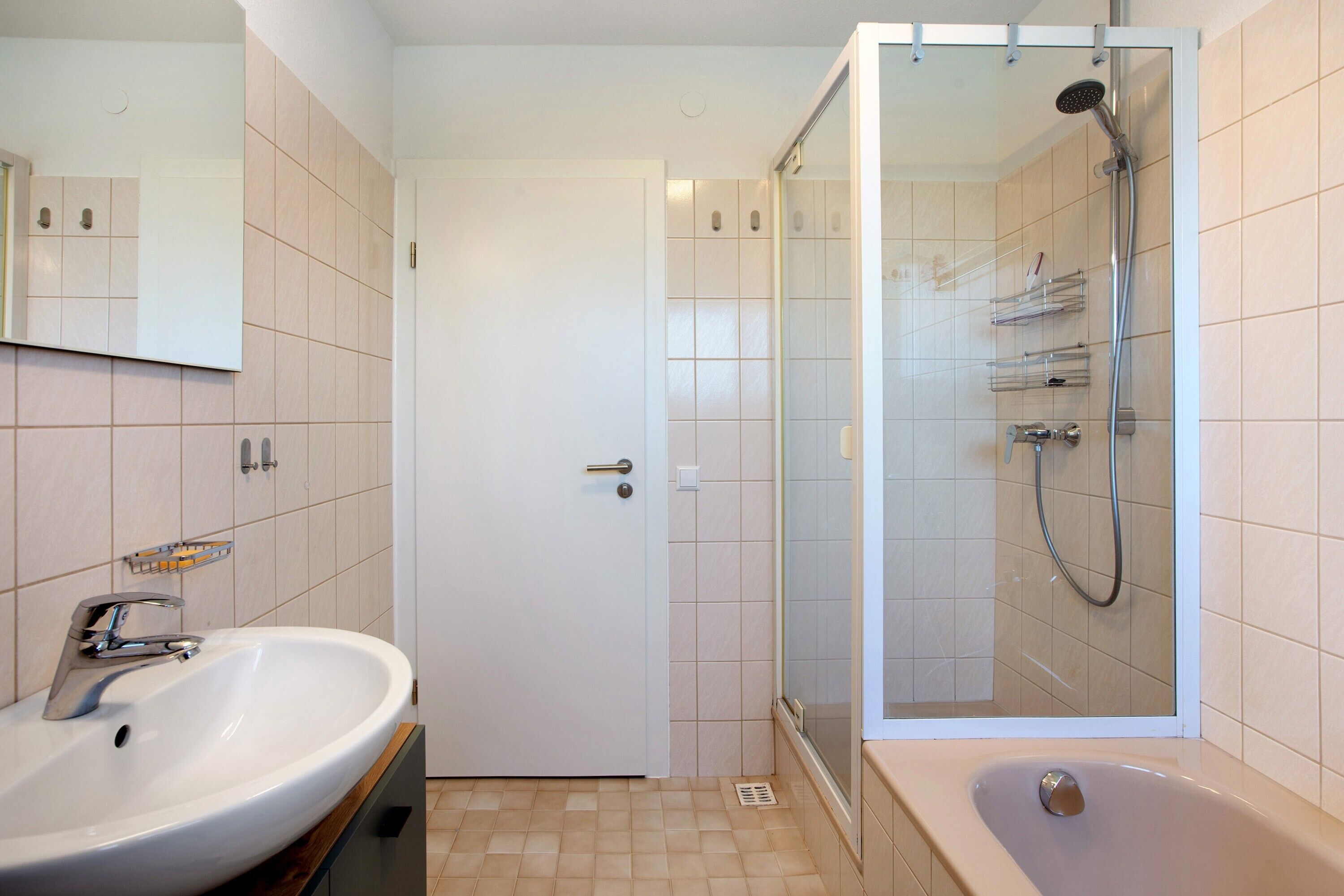 A bathroom with a sink, mirror, shower, and door.