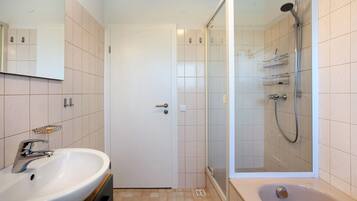 A bathroom with a sink, mirror, shower, and door.