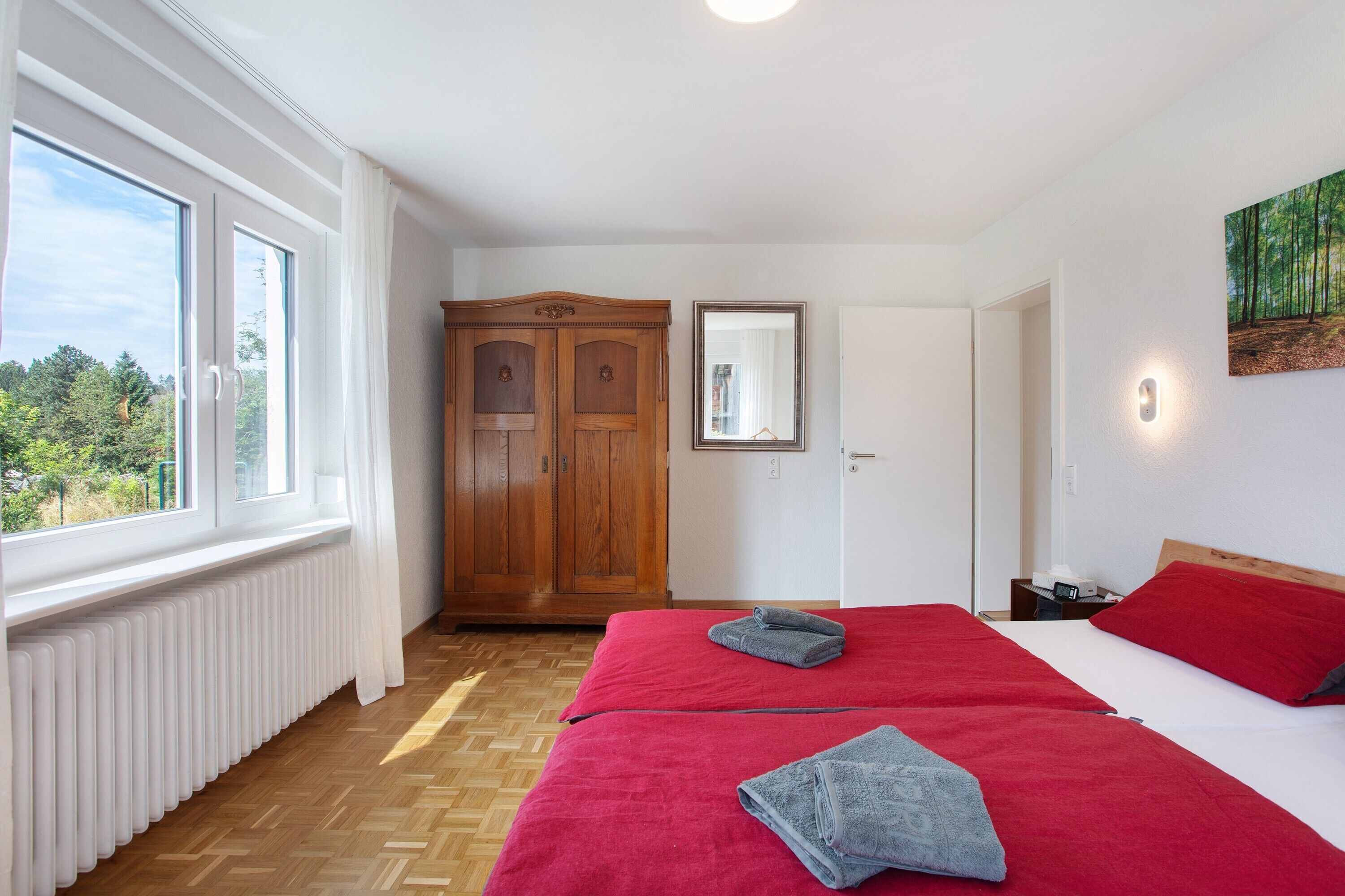 Slaapkamer met twee bedden, een houten garderobe, een radiator, een raam met uitzicht en een schilderij aan de muur.