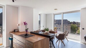 A modern kitchen with a central island, dining area with chairs, large windows, and a view of buildings. - Apartment 'Yiwoo Home' with Private Terrace, Balcony and Wi-Fi (Gießen)