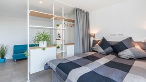 A modern bedroom with a bed, a blue sofa, a white shelving unit, and a grey curtain. - Apartment 'Yiwoo Home' with Private Terrace, Balcony and Wi-Fi (Gießen)