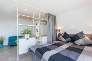 Une chambre à coucher moderne avec un lit, un canapé bleu, une étagère blanche et un rideau gris.