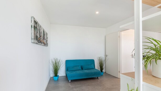A modern room with a teal sofa, white walls, and a door leading to another area. - Apartment 'Yiwoo Home' with Private Terrace, Balcony and Wi-Fi (Gießen)